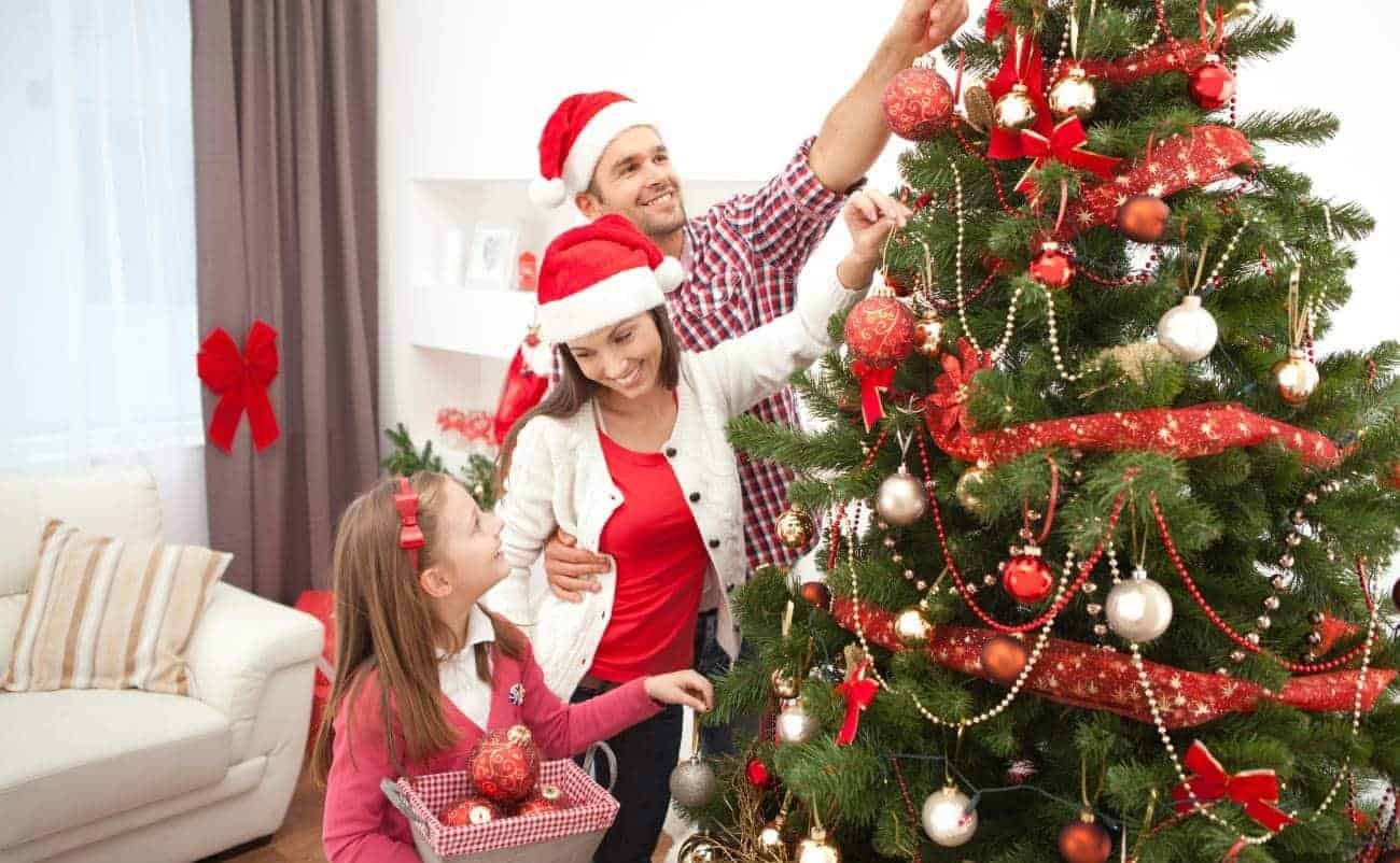Festive family decorating Christmas tree with ornaments, ribbons, and lights, celebrating holiday spirit and joy during the Christmas season.