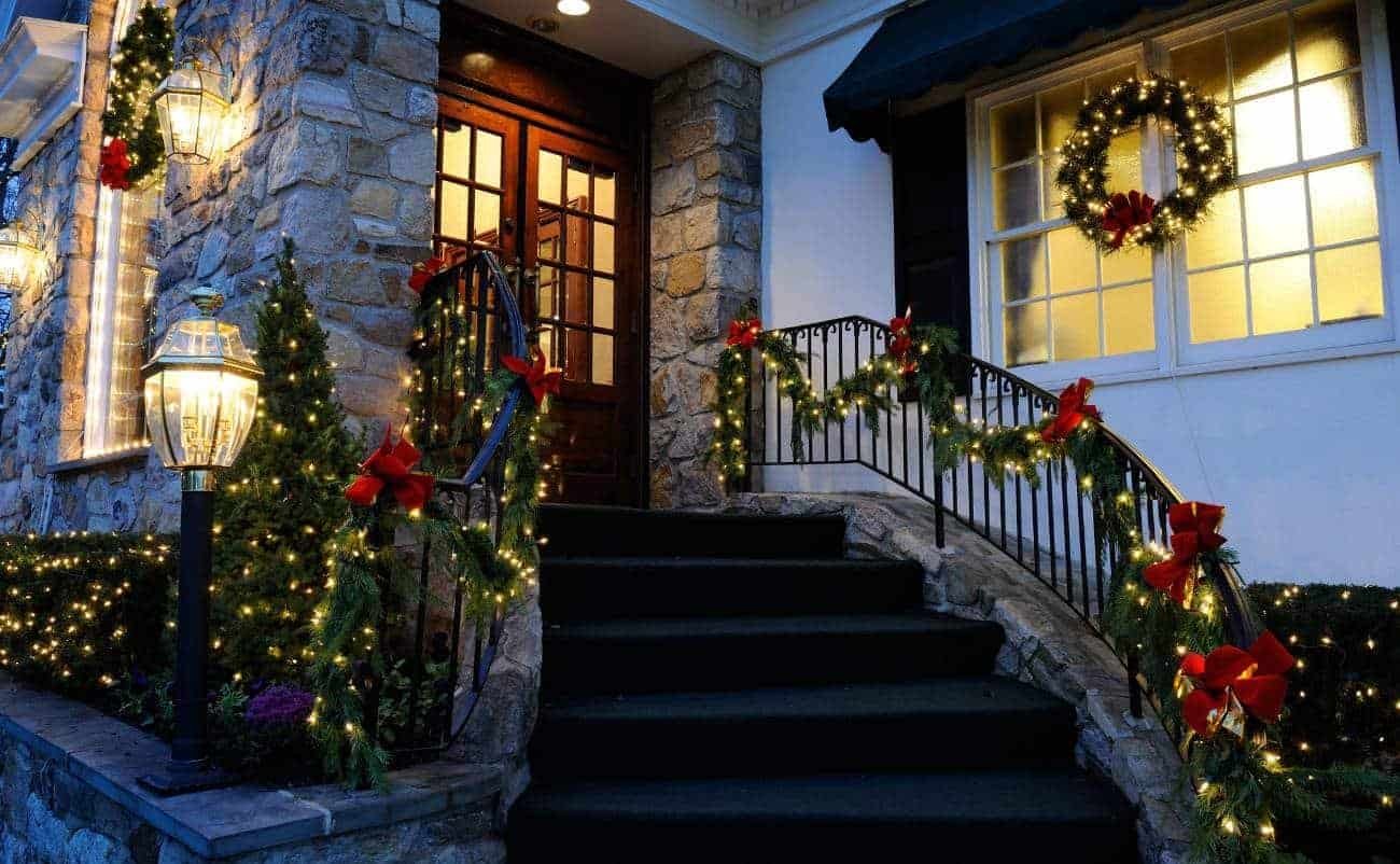 Brightly decorated Christmas house with wreath, garlands, lights, and red bows on steps and porch, celebrating holiday spirit and faith through festive decor.