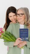 Joyful woman and elderly woman sharing a happy moment with flowers and a thank you card, emphasizing faith, gratitude, and family love; perfect for promoting My Bible Song for Christian families.