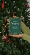 Beautiful Christmas card featuring a biblical verse, held in front of a decorated Christmas tree with lights and ornaments, conveying holiday cheer and faith.