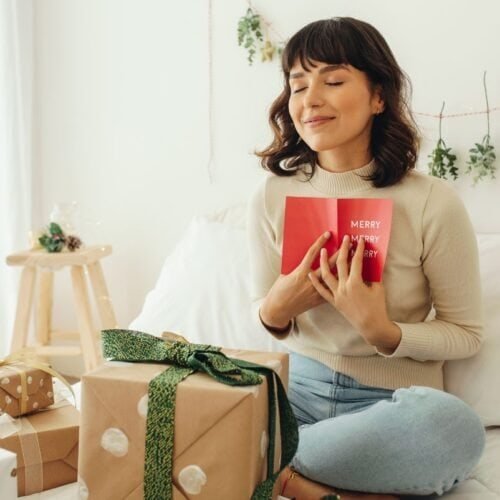 Celebrating Christmas with a joyful woman holding a Christmas card, surrounded by gift boxes and festive decorations, capturing the spirit of holiday cheer and spiritual gratitude.