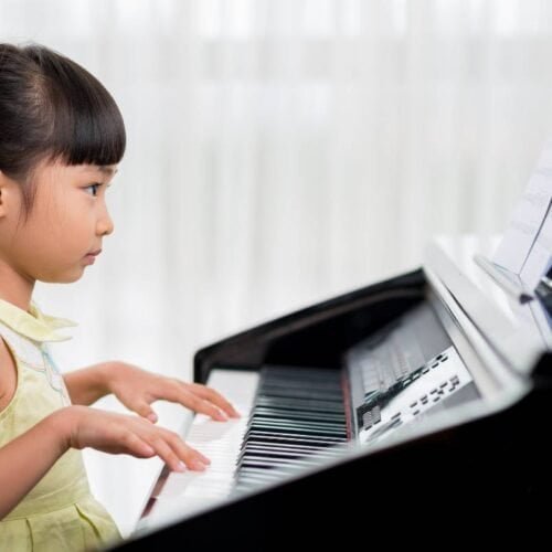 A young girl playing the piano, focusing on learning and singing biblical songs from My Bible Song platform for children.