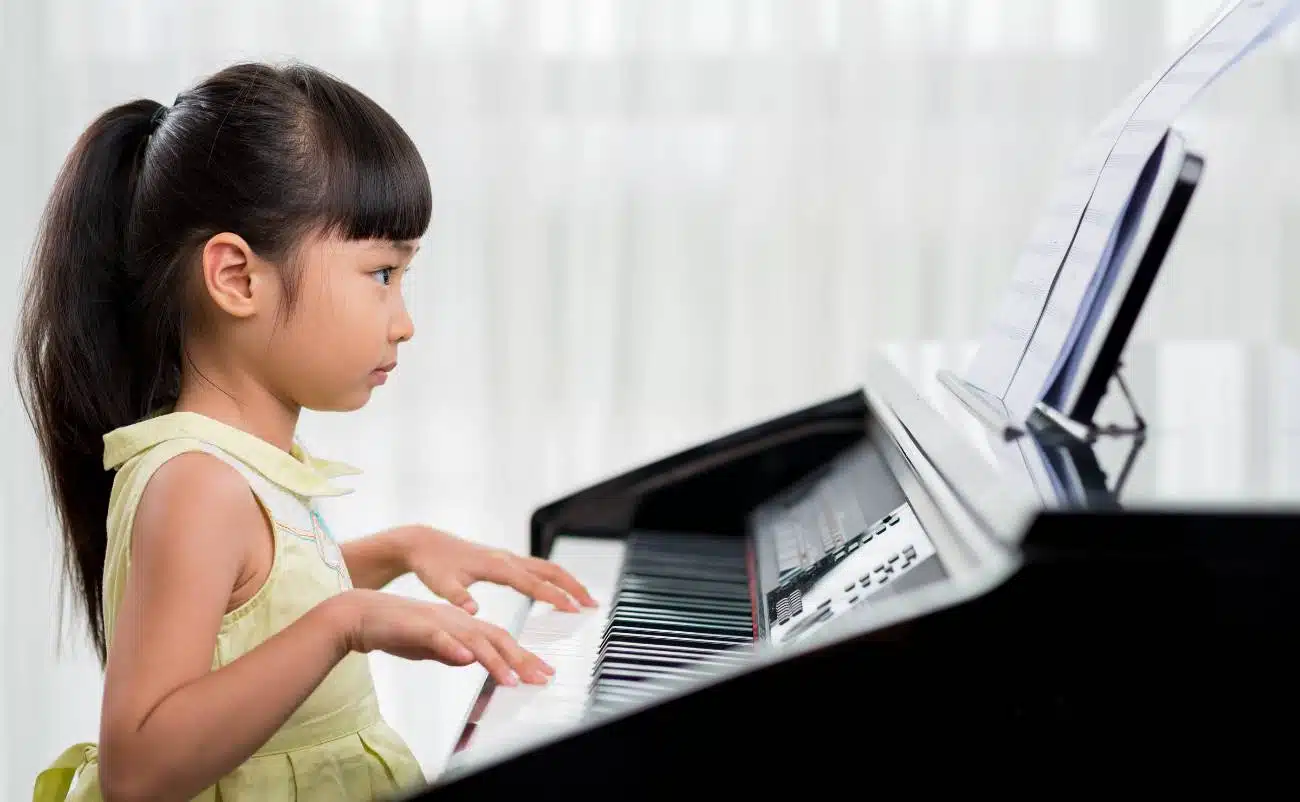 A young girl playing the piano, focusing on learning and singing biblical songs from My Bible Song platform for children.