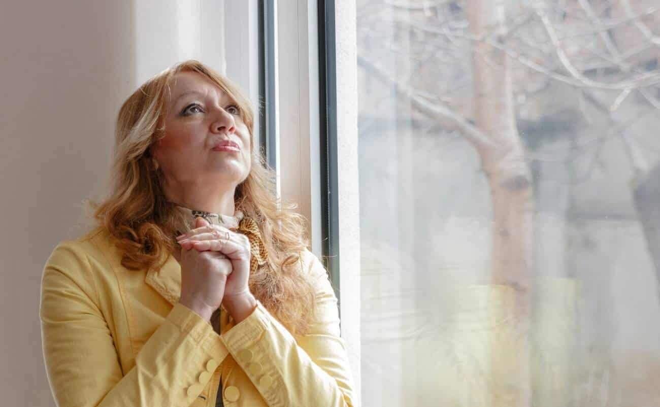 Reflective woman praying and worshiping by a window, seeking faith and spiritual connection, representing devotion, prayer, and trust in God's guidance. Great image for faith-based themes and Christian worship.
