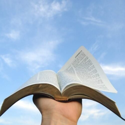 Empowering Bible Motivational Quotes in Gujarati: Uplift Your Spirit Today! My Bible Song 2025 Bible open in hand against blue sky with clouds, symbolizing faith and spiritual growth, promoting biblical teachings and Christian devotion.