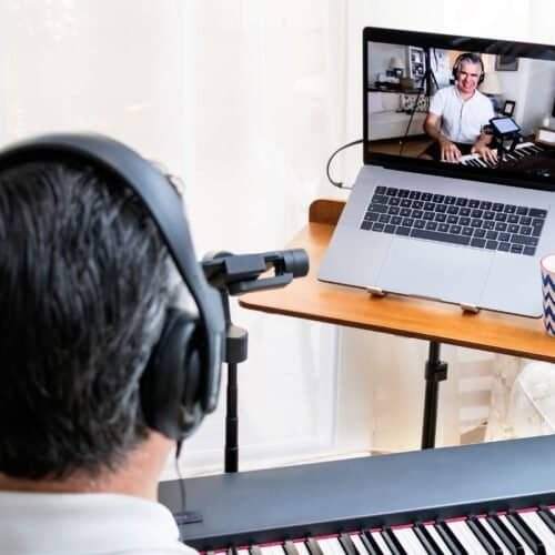 Recorded man in headphones playing keyboard while participating in a virtual church singing session on laptop.