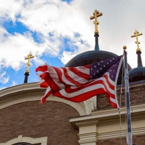 Discover the Heartfelt Lyrics of God Bless America A Deep Dive into Its Meaning and Legacy My Bible Song 2025 American flag waving in front of a church with golden crosses under a partly cloudy sky, symbolizing faith, patriotism, and spirituality for Christian church worship and religious community.