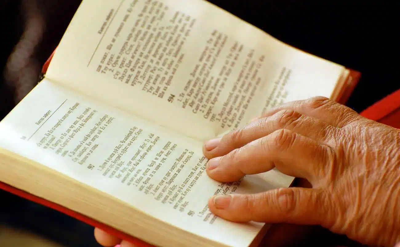 Aged hand holding open Bible page, highlighting scripture reading, worship, gospel, faith, and spiritual growth.