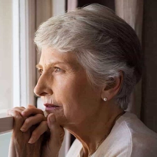 Elderly woman looking out a window with hope and peace, contemplating faith and prayer, symbolizing spiritual reflection and trust in God for inspiration and guidance in daily life, representing religious devotion and inner peace.