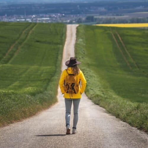 Walking woman on rural country road with lush green hills, representing faith and guidance, ideal for inspirational and religious journeys to connect with God and spiritual growth.