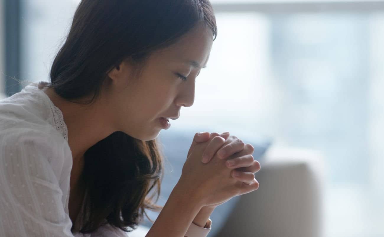 A woman praying peacefully with her hands clasped, reflecting faith and devotion, promoting spiritual connection and Christian worship through prayer and prayer music.