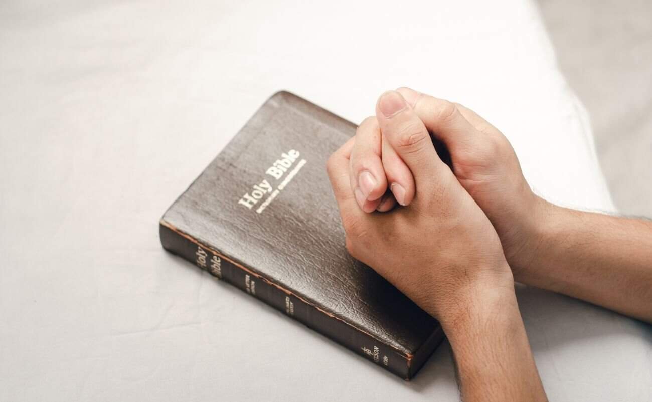 Bible praying hands on a black Holy Bible for faith, worship, and religious devotion.