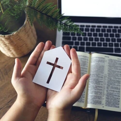 What Does Bible Verse 12:12 Teach? A Simple Lesson of Hope and Faith My Bible Song 2026 High-quality photo of a person holding a cross card with an open Bible, laptop, and potted plant on wooden table, representing Christian worship and Bible study, ideal for My Bible Song online resources.