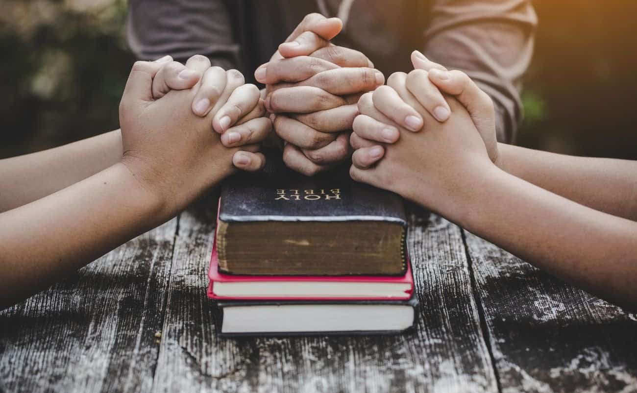 Praying hands over Bible and prayer books, symbolizing faith and spirituality, with a focus on Christian prayer and biblical devotion.