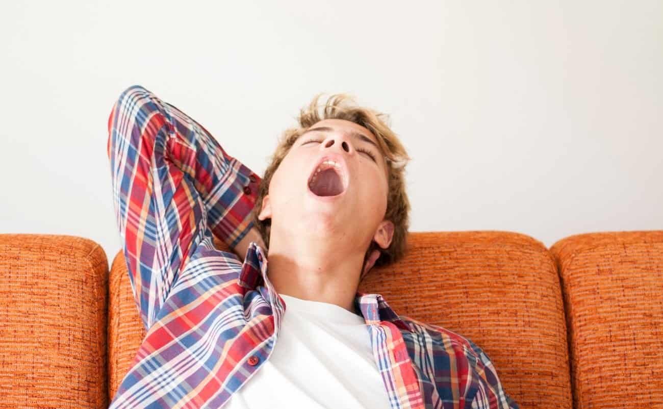 Yawning young man relaxing on a sofa, symbolizing rest and reflection which can be connected to spiritual renewal through Bible songs.