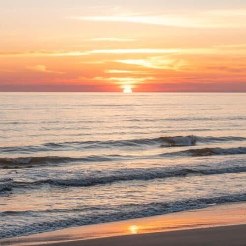 Sunset over ocean with colorful sky, peaceful waves, and sandy beach, perfect for inspiring Christian music and worship moments.
