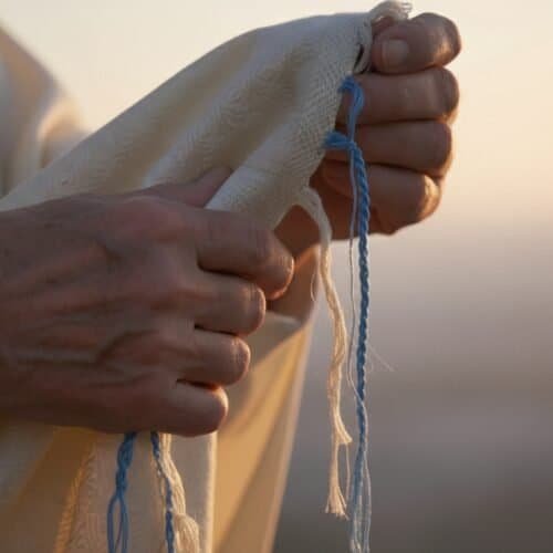 Hands holding prayer shawl with blue and white tassels during sunset, symbolizing faith, prayer, and spirituality in Christian worship. Ideal for religious devotion, prayer, and Bible inspiration.
