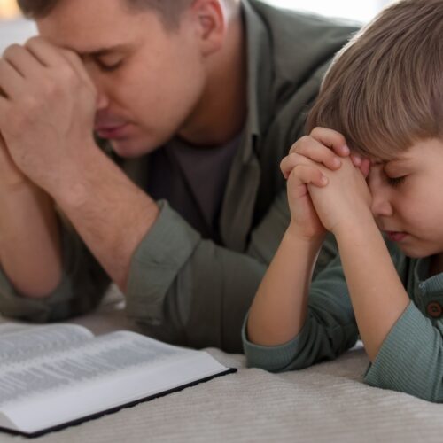 Father and son praying together with open Bible, emphasizing faith, prayer, and family devotion.