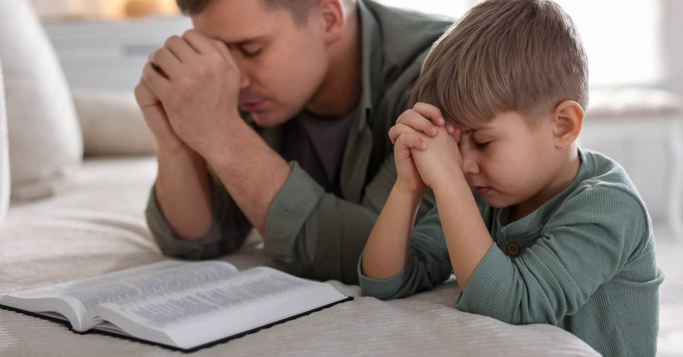 Father and son praying together with open Bible, emphasizing faith, prayer, and family devotion.